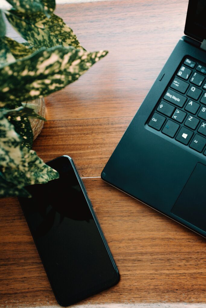 Top view of a smartphone and laptop on a wooden desk with a plant, ideal for tech themes.